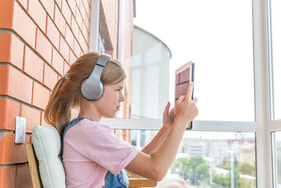 Side view of girl using digital tablet sitting in balcony