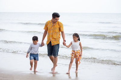 Father with children walking at beach against sky