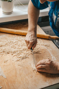 A woman cuts the dough with a knife and makes homemade noodles in the kitchen.