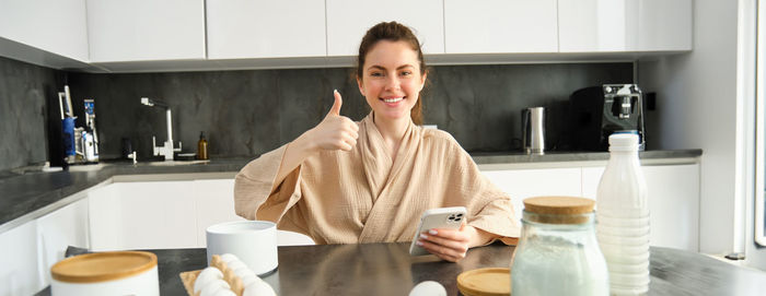 Young woman using mobile phone while sitting in kitchen