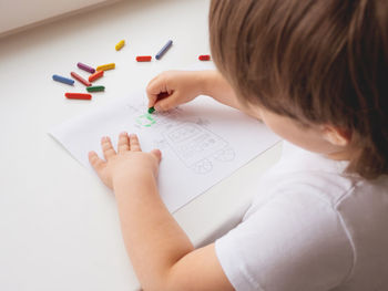 Toddler draws colorful robot. kid uses wax crayons to paint it. coloring to train fine motor skills.