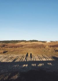 Shadow of couple on field against clear sky