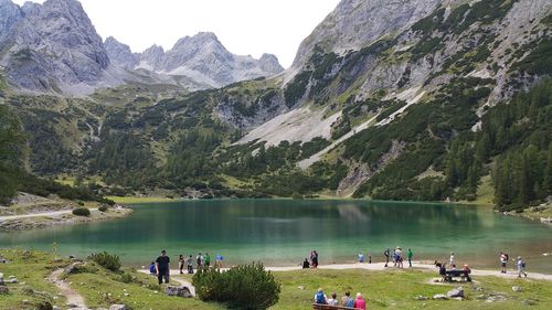 Tourists at lakeshore by mountains