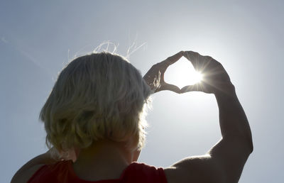 Rear view of woman making heart shape with hands against sky