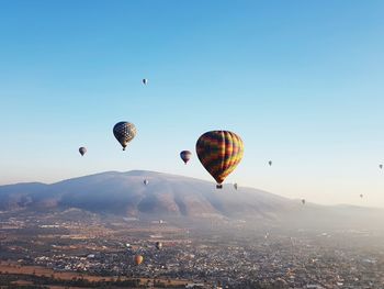 Hot air balloons flying over landscape against clear blue sky