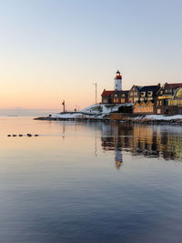 Buildings by sea against clear sky during sunset