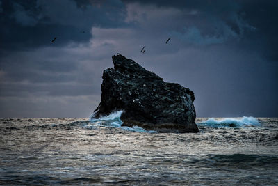 Storm clouds and waves hitting a rock