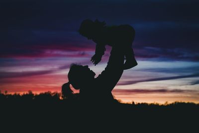 Silhouette mother playing with baby against sky during sunset