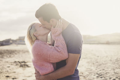 Couple kissing at beach against sky during sunset