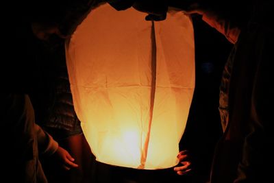 Midsection of male friends holding illuminated paper lantern at night