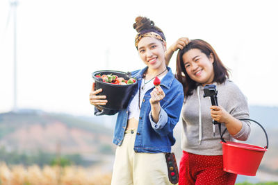 Portrait of smiling young women with strawberries against sky