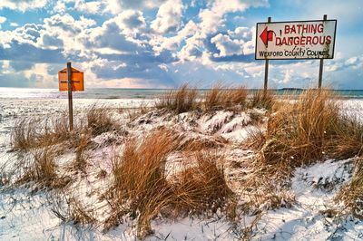 Information sign on snow covered landscape against sky