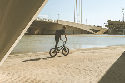 Man riding bicycle by river in city