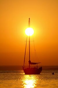 Silhouette sailboat in sea against orange sky