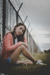 Portrait of teenage girl sitting on grassy field against fence