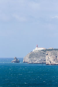 Lighthouse on cliff by sea against sky