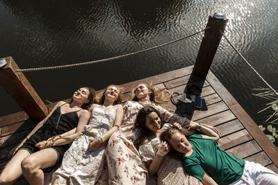 Smiling young friends with eyes closed lying on pier