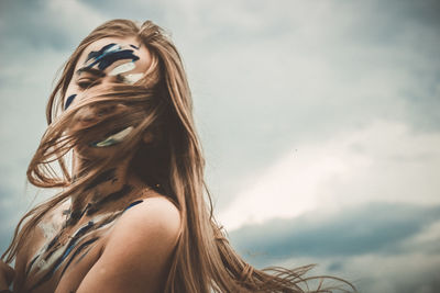 Portrait of young woman with face paint standing against sky