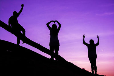 Silhouette people gesturing against sky during sunset