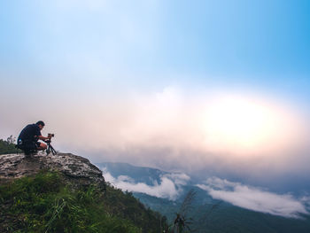 Man sitting on mountains against sky during sunset