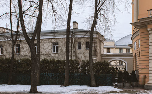 Bare trees by buildings against sky during winter