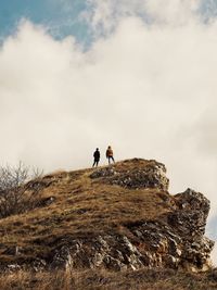 Low angle view of people standing on rock against cloudy sky
