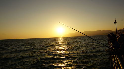 Man fishing in sea against sky during sunset