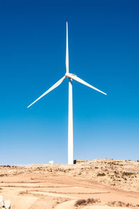 Windmill on desert against clear blue sky