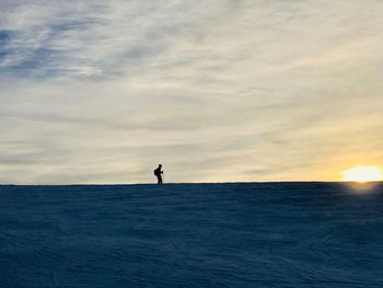 Silhouette man standing in sea against sky during sunset