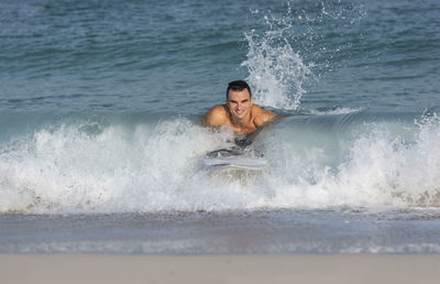 Full length of shirtless man splashing water in sea