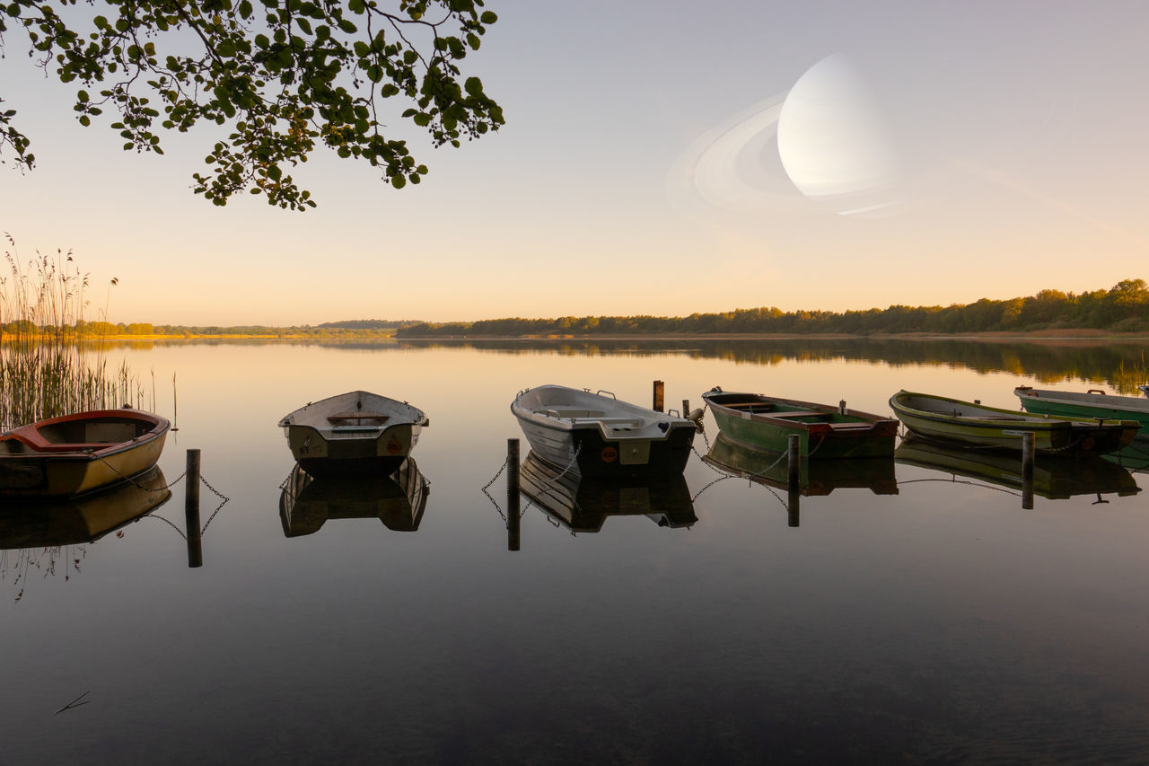 BOATS MOORED IN LAKE AT SUNSET