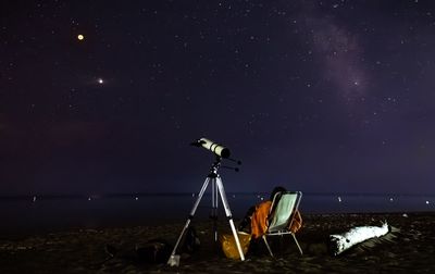 Telescope by deck chair against sky at night