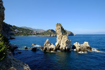 Rock formation in sea against clear blue sky