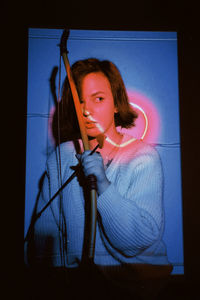 Portrait of young woman looking away while standing against blue wall