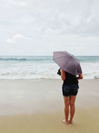 Rear view of woman standing on beach against sky