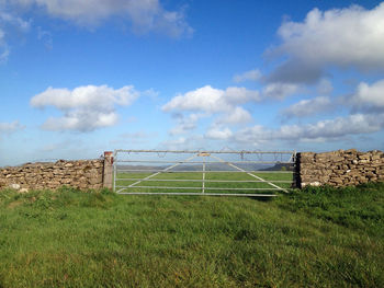 Closed gate on grassy field against sky
