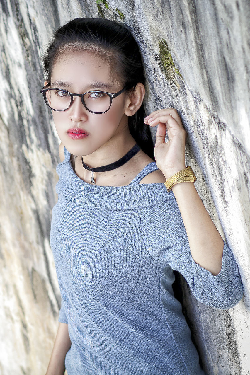 one person, glasses, portrait, blue, eyeglasses, photo shoot, child, women, spring, looking at camera, fashion, casual clothing, childhood, leisure activity, young adult, portrait photography, waist up, female, nature, adult, hairstyle, rock, outdoors, lifestyles, day, standing, person, wall - building feature, emotion, clothing, human face, sports, teenager, front view, looking