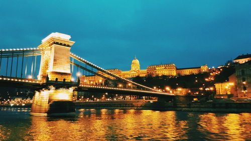 Low angle view of illuminated chain bridge over river against sky in city