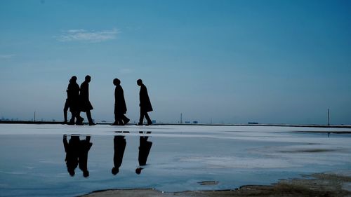 Silhouette people standing by sea against sky