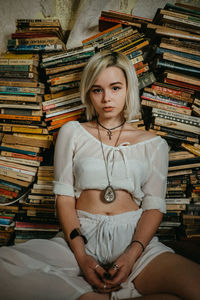 Portrait of young woman sitting against stacked books