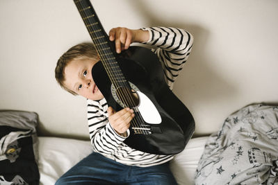 Portrait of boy with down syndrome holding guitar sitting in bedroom
