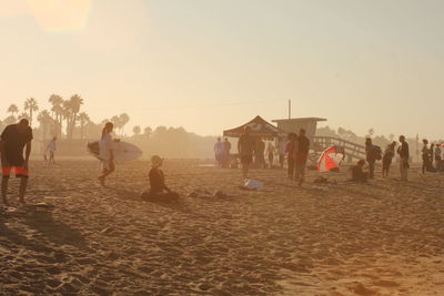 People at beach against sky during sunset