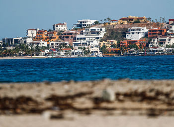 Sea and buildings in city against clear sky