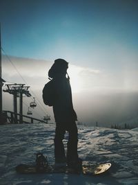 Silhouette woman standing on snow covered field against sky during winter