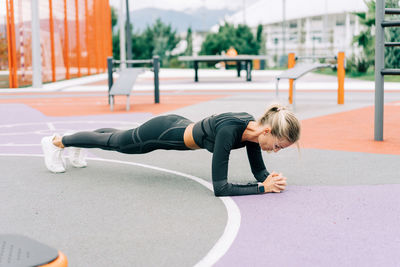 A woman athlete stands in a plank on the sports ground during a workout.