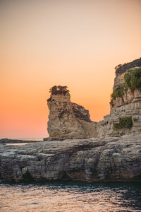 Rock formation by sea against sky during sunset