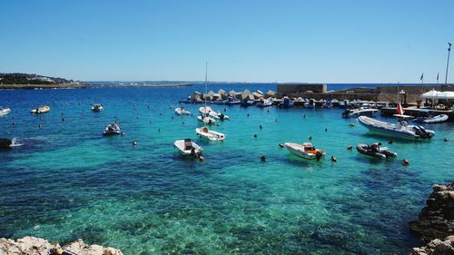 Boats moored on sea against clear blue sky