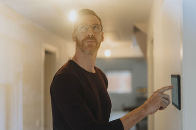 Mature man adjusting room lights through digital tablet while standing at smart home