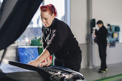 Female mechanic repairing car while colleague standing in background at auto repair shop