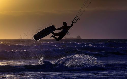 Silhouette person on wakeboard over sea during sunset